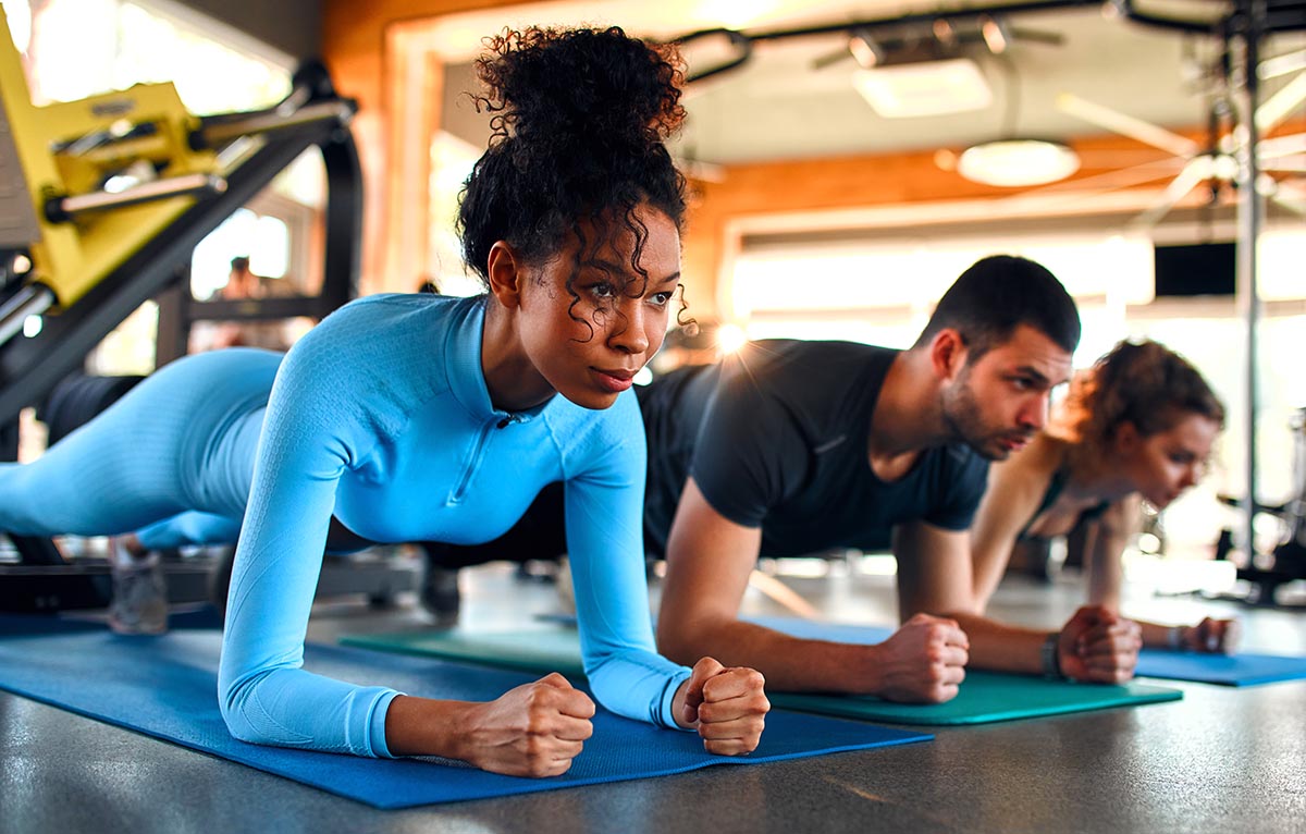 three fit people doing planks on rubber mats in a gym