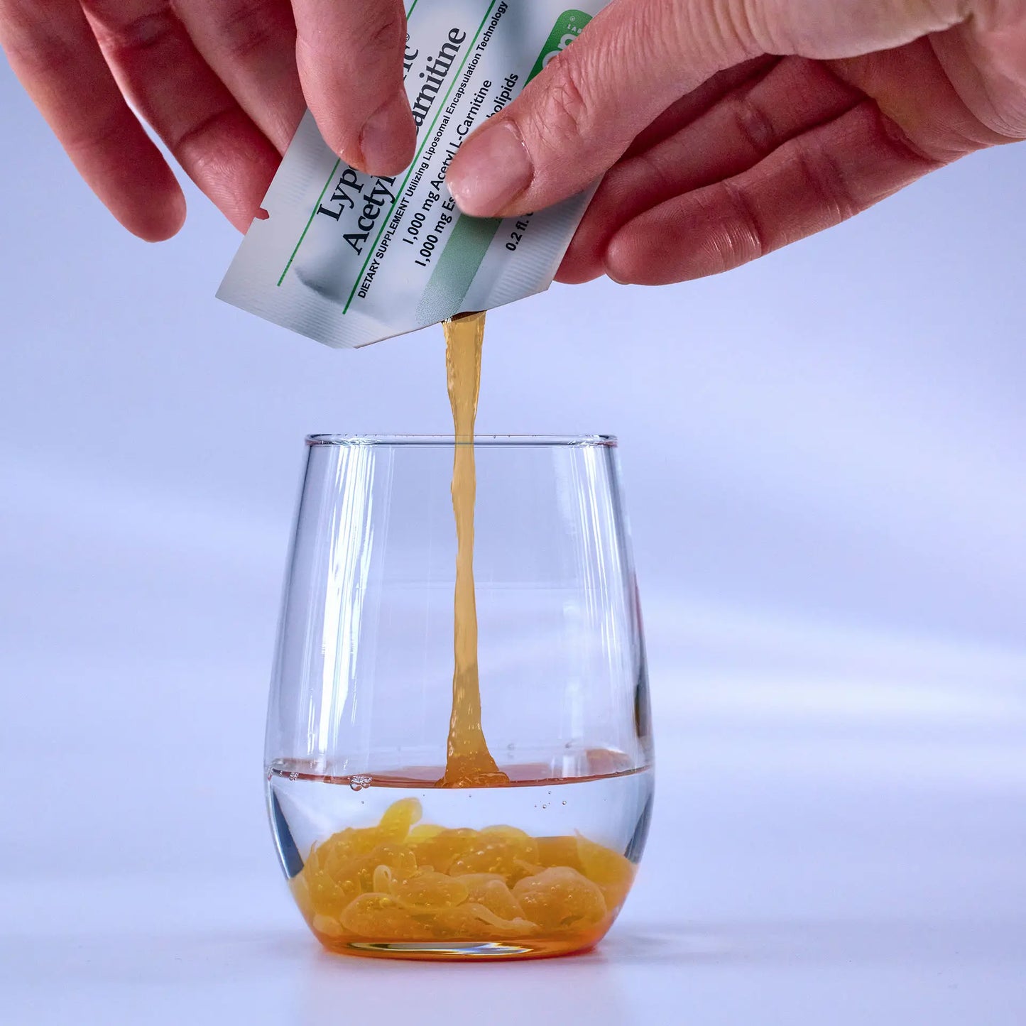 hands squeezing Lypo-Spheric Acetyl L-Carnitine into a shot glass