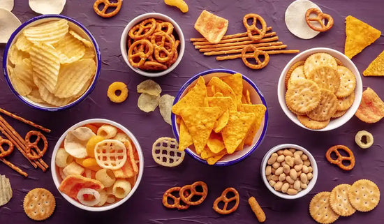 small bowls of processed chips, crackers, and pretzels on a dark surface