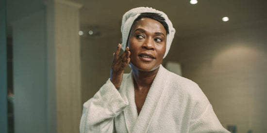 woman in robe applying skincare products on her face