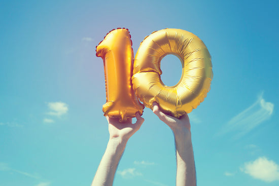 hands in front of sky holding 1 and 0 balloons