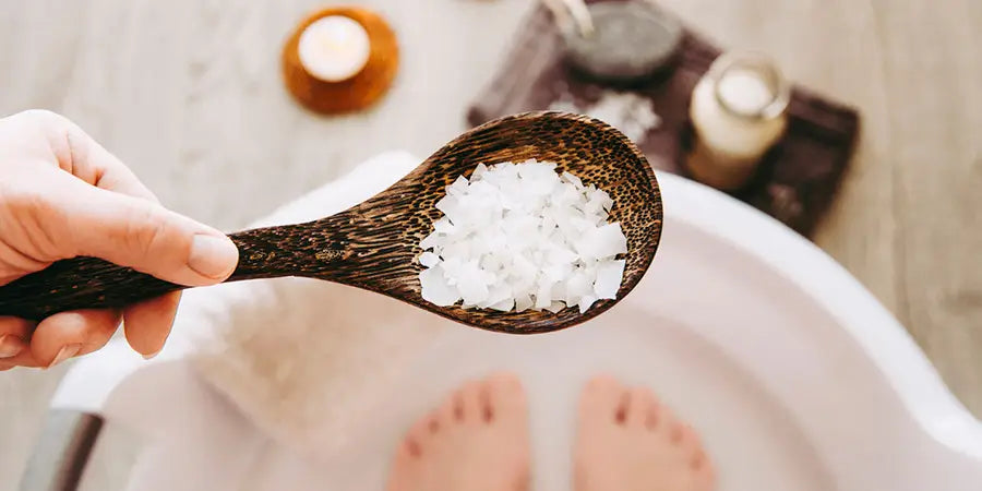 hand holding epsom salts over feet in a tub for a transdermal magnesium soak