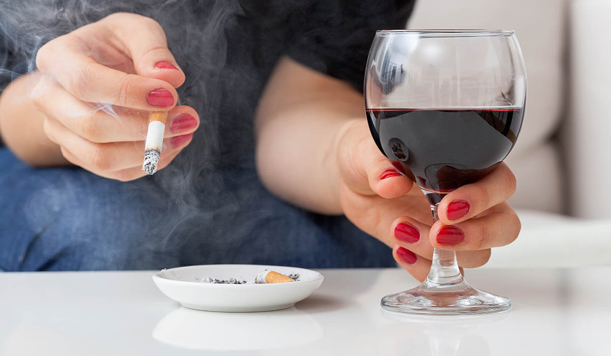 close up of woman's hands holding lit cigarette and red wine glass