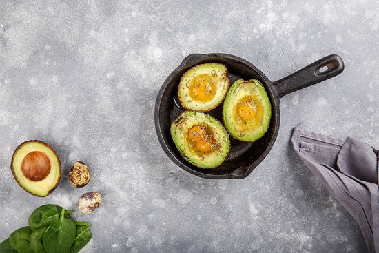 Avocado egg boats in cast-iron pan on gray background