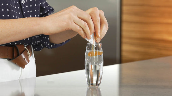 woman's hands squeezing a packet of liposomal vitamin c into a shot glass