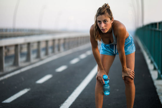 woman resting after a run with a bottle possibly containing drinkable workout recovery foods