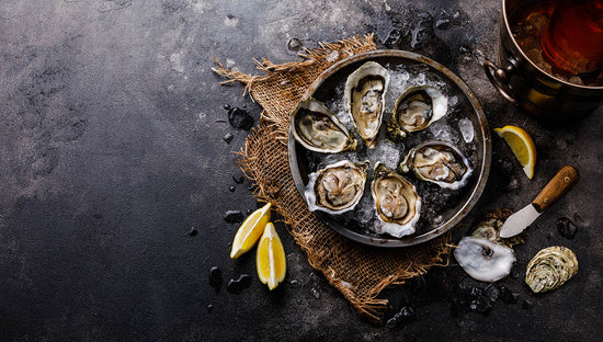 Open shucked fresh Oysters — a good source of zinc — with lemon and Rose Wine in ice bucket on dark background copy space