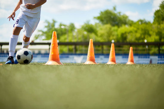 soccer player kicking a ball around cones