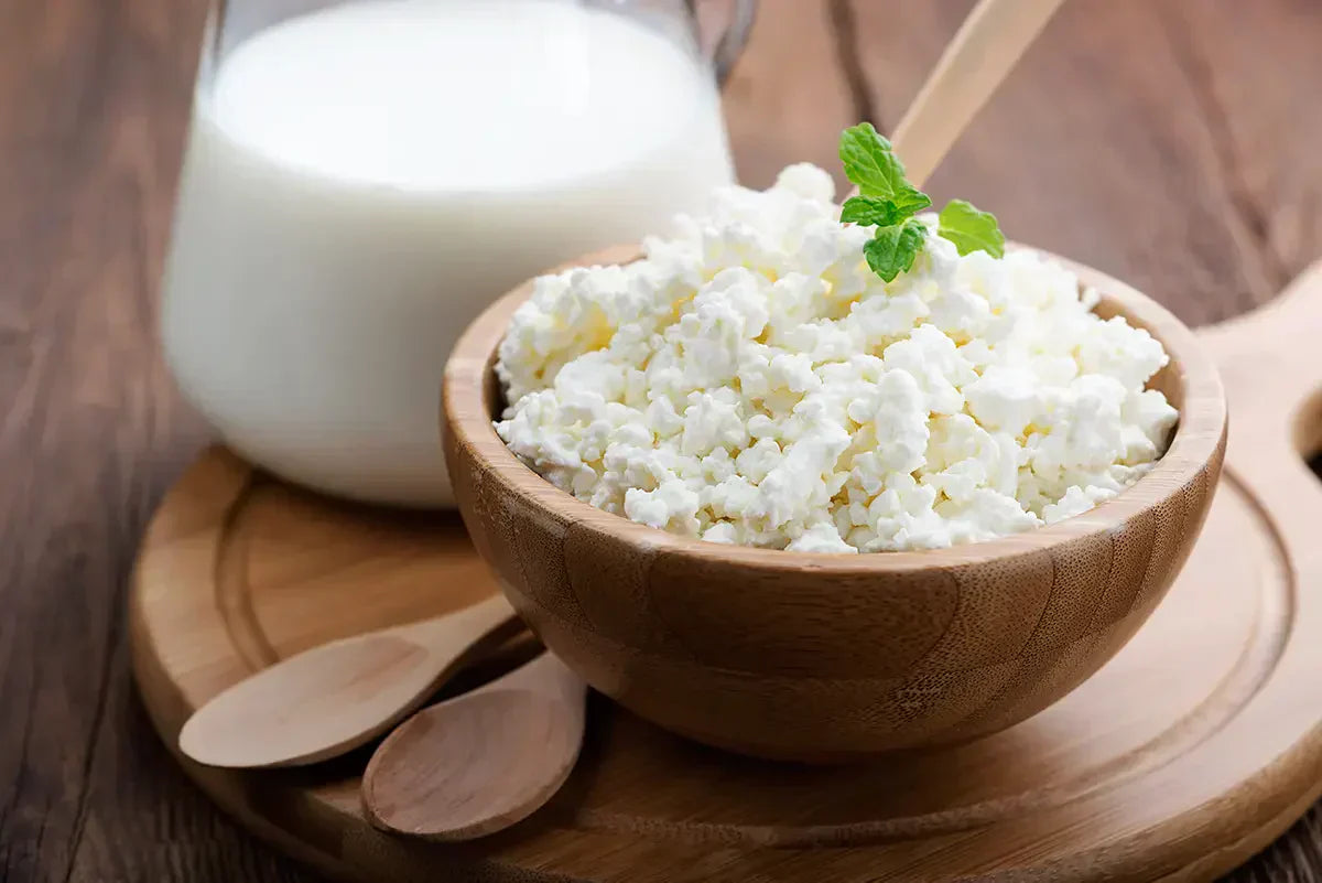wooden bowl of cottage cheese on a board with spoons and glass of milk