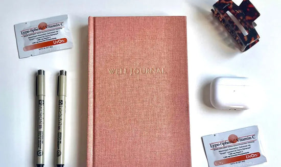 bird's eye photo of The Well Journal, pens, and packets of Lypo-Spheric Vitamin C on a white surface