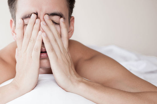 stressed man lying in bed with hands in front of his face