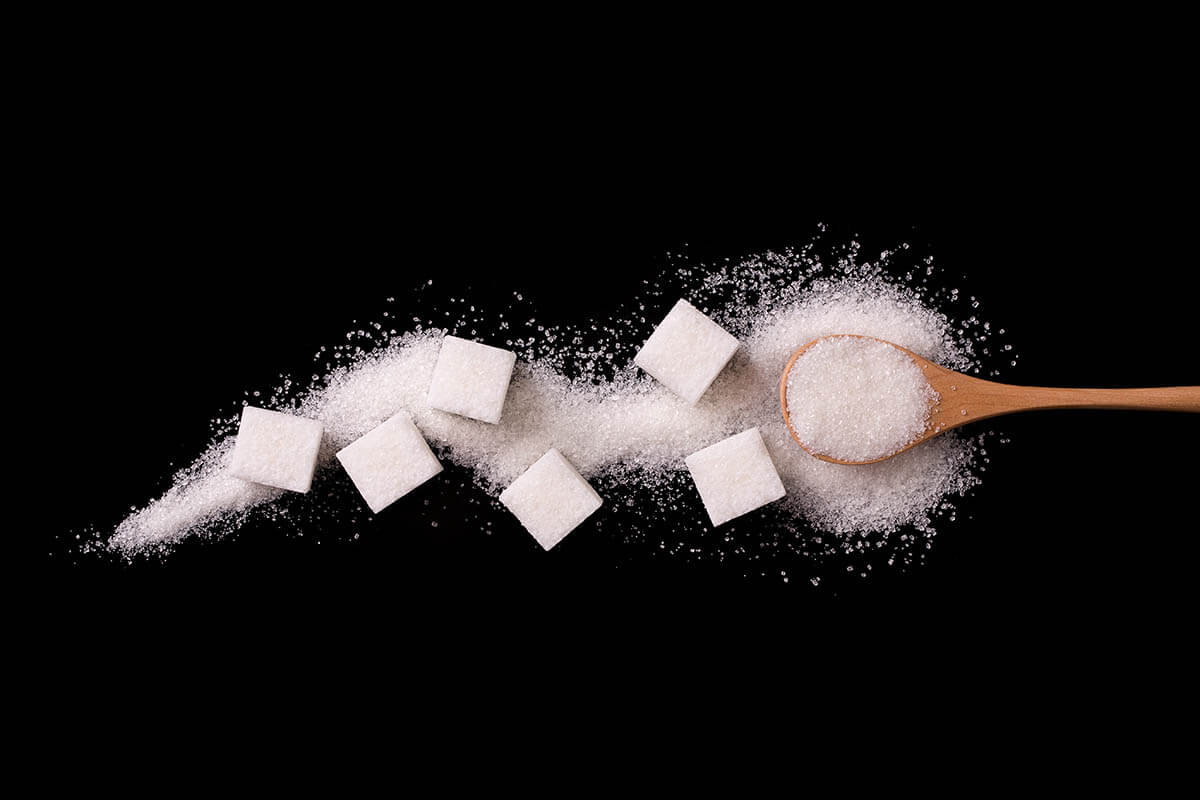 Sugar scattered from wooden spoons on a black background. Excess sugar like in these cubes can deplete vitamins and minerals