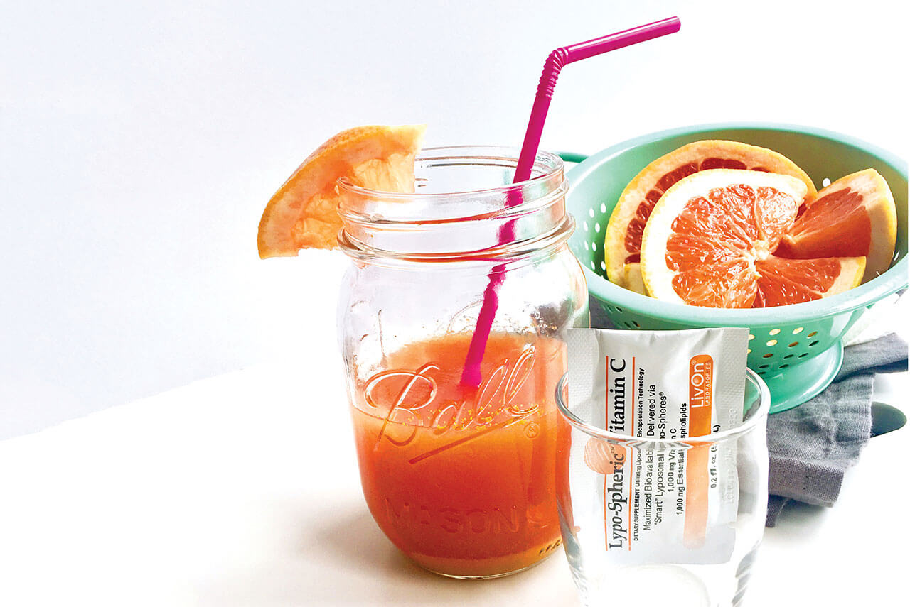 mason jar filled with summer skin drink, bowl of grapefruit, and empty shot glass with packet of lypo spheric vitamin c
