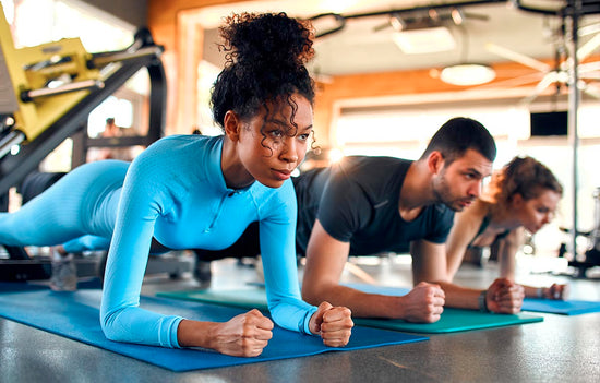 three fit people doing planks on rubber mats in a gym