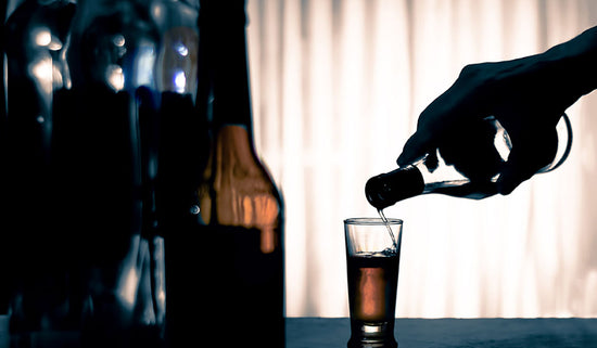 silhouetted hand pouring alcohol in to a glass