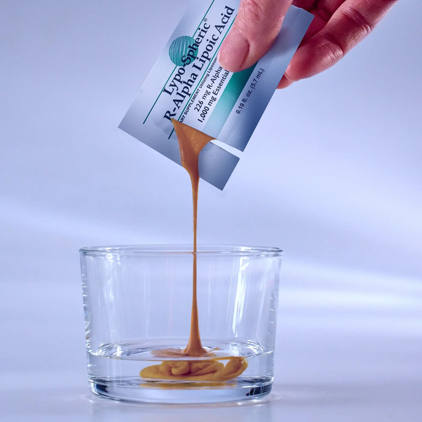 A hand holds a packet of Lypo-Spheric® R-Alpha Lipoic Acid and pours  goo into shot glass of water